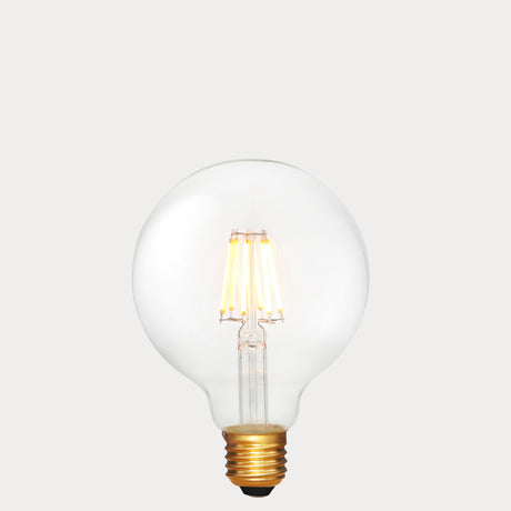 Dulora 6W E27 LED globe bulb in clear glass with 24V compatibility, glowing with 2200K extra warm white light.